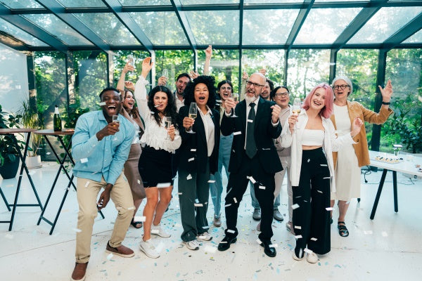 Group of people celebrating with drinks indoors, surrounded by large windows.