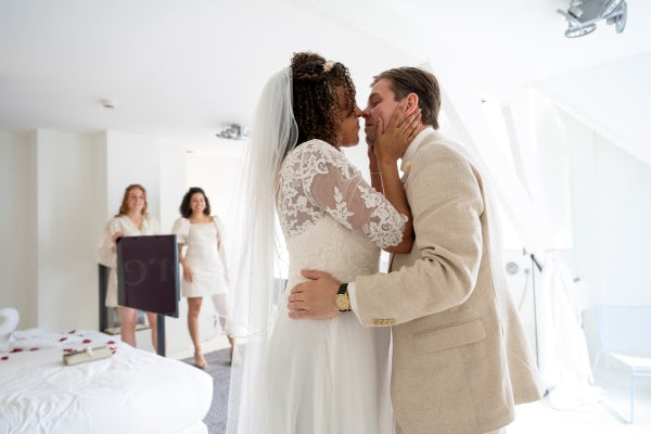 Couple kissing in a bedroom with two women in the background.