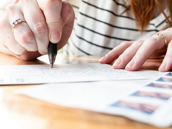 Person writing on a piece of paper with a pen, wearing a striped shirt.